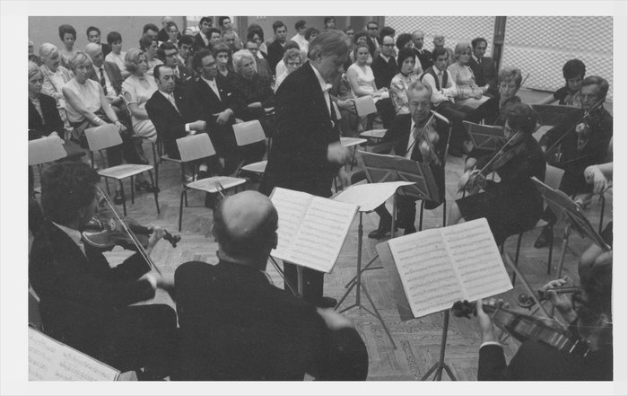 Dirigent a hráči orchestru při koncertě před publikem, historická fotografie