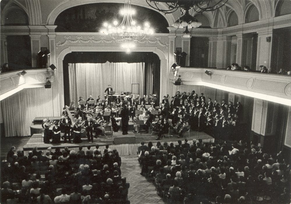 Historická fotografie koncertu orchestru před zaplněným sálem